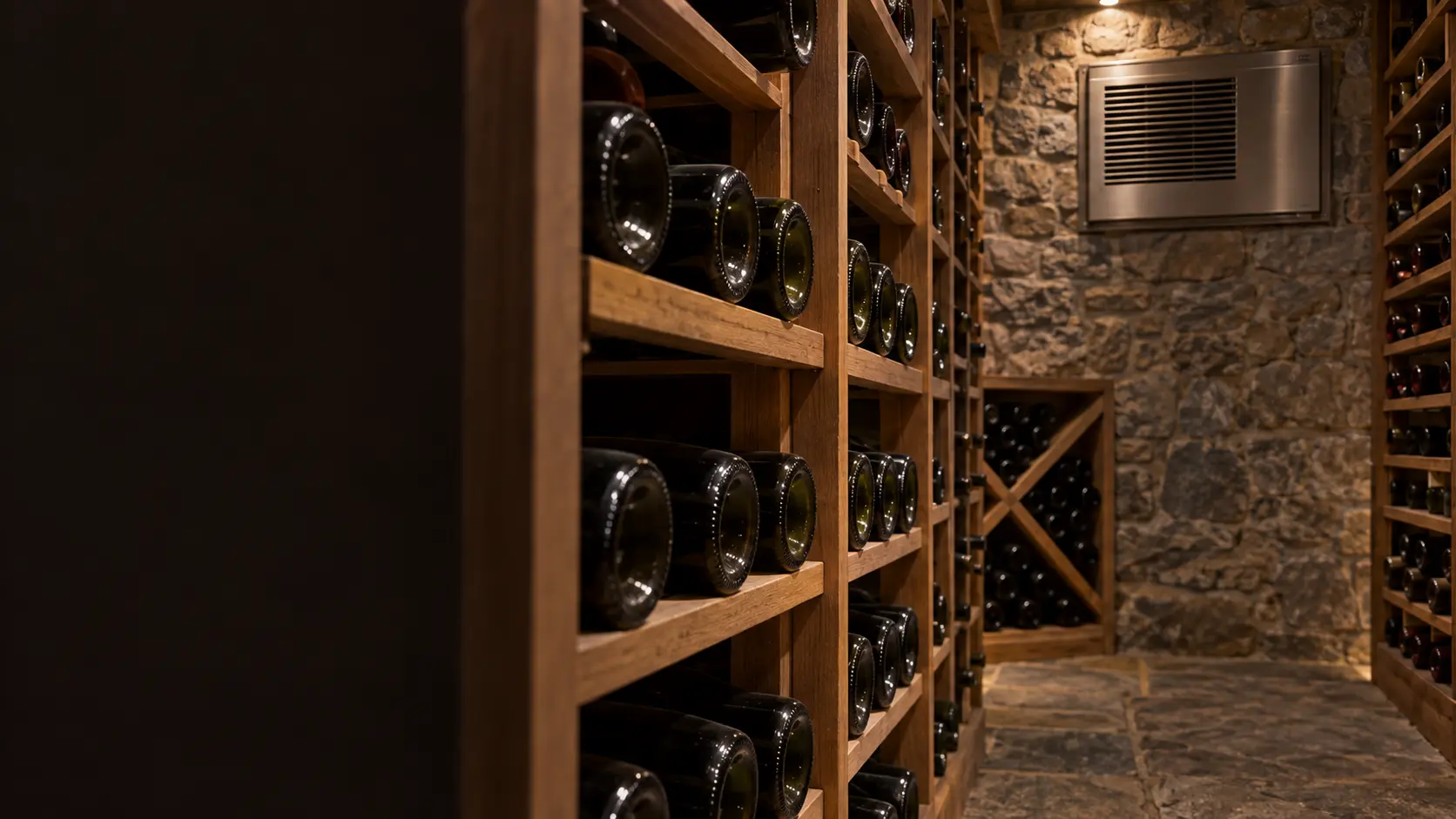 A wine cellar with a through-wall cooling unit and stone walls, seen close and low along the racks.