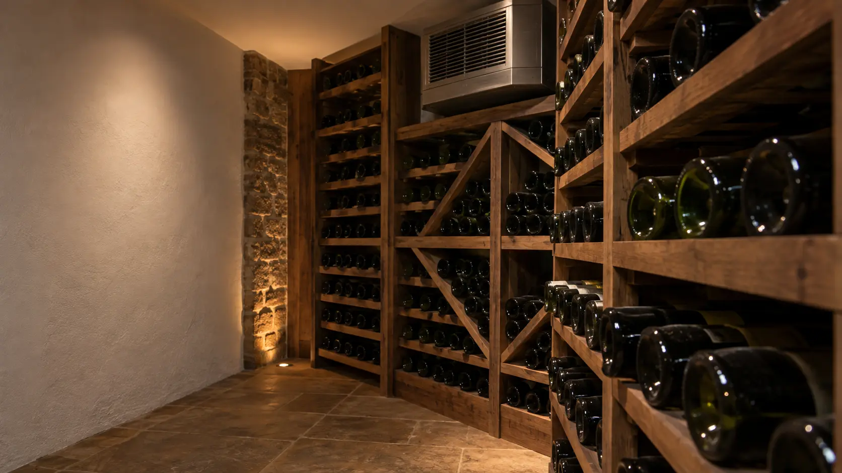 A wine cellar with a through-wall cooling unit and white plaster walls, seen close and low along the racks.