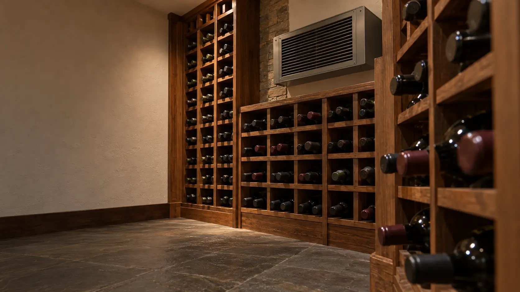 A wine cellar with a through-wall cooling unit and white plaster walls, seen close and low along the racks.