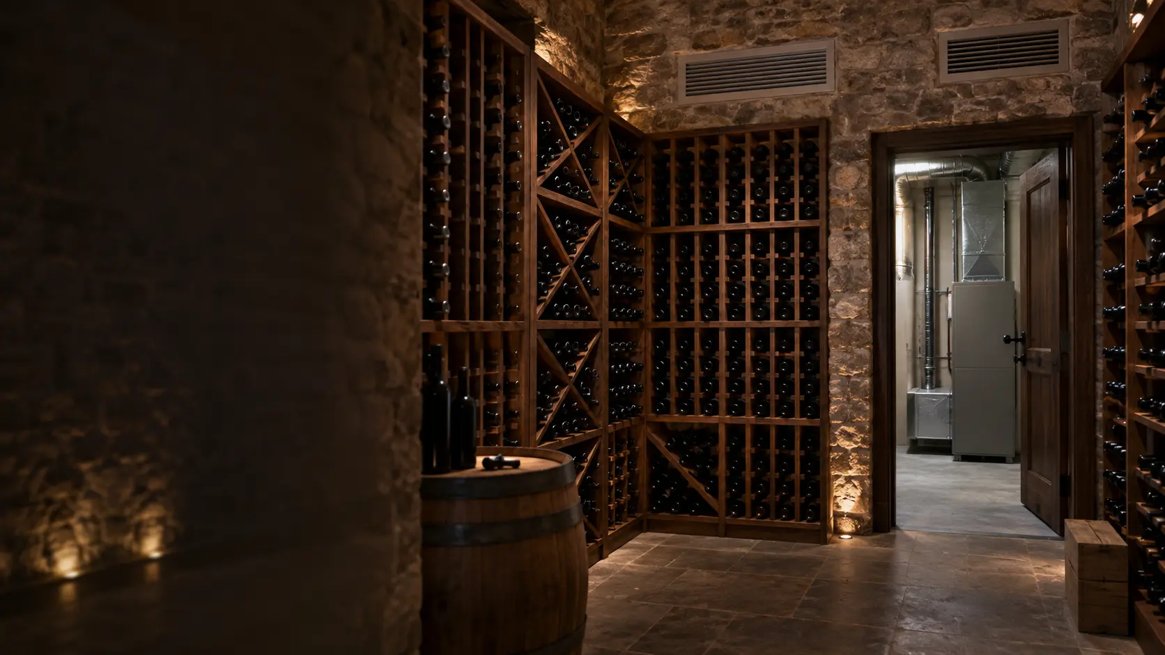 A finished stone wine cellar with wooden racks of unlabeled bottles, a flush supply grille and return grille of a ducted cooling unit set into the upper wall, and through an open doorway the plain mechanical room beside it.